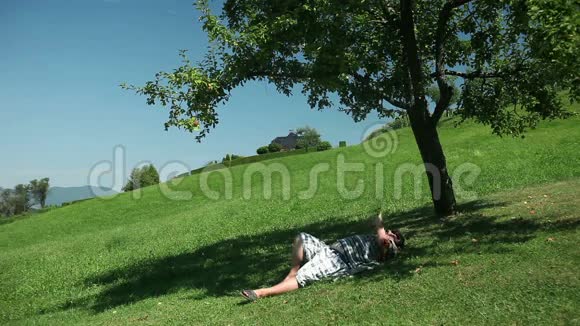一个人躺在树下在巨大的草坪上视频的预览图