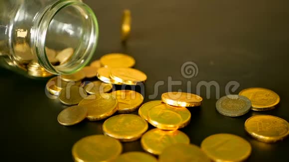 用黑桌上的金币和旋转的便士来特写静止的生活黄色的硬币从罐子里掉了出来视频的预览图