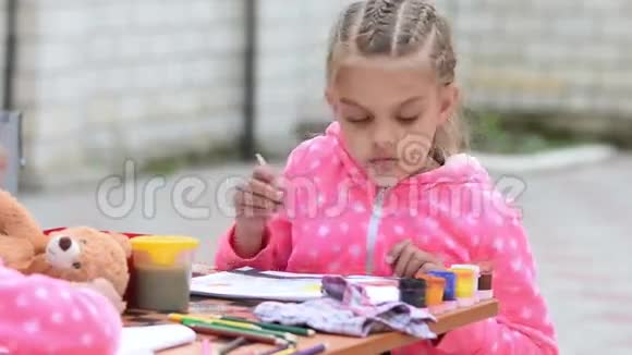 七岁的女孩硬灌篮刷在一个罐子里在相册上画着水彩颜料和另一个女孩坐在桌子旁视频的预览图