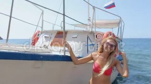 戴墨镜的金发碧眼在沙滩上的船边摆着粉色比基尼视频的预览图