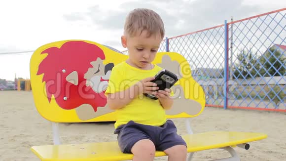 一个小男孩坐在长凳上玩电话视频的预览图