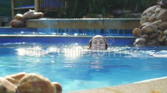 在阳光明媚的日子里布鲁内特可爱的女人在游泳池里慢动作地享受水在享受美丽的阳光效果的假期里视频的预览图