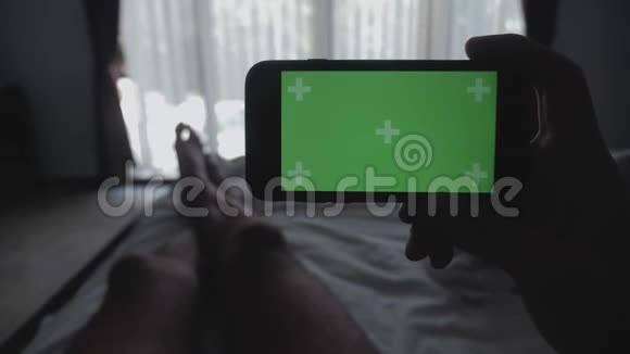 合上躺在床上的年轻人手里拿着智能手机绿色屏幕彩色键绿色屏幕分享真实的社交视频的预览图