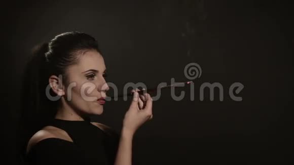 美丽的女人在黑色背景上的喉舌里抽烟视频的预览图