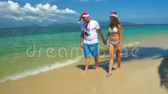 浪漫的情侣漫步在圣诞老人小屋的海滩上在炎热的国家庆祝新年视频的预览图