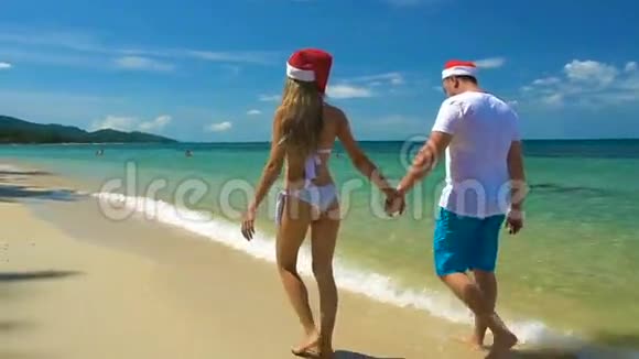 浪漫的情侣漫步在圣诞老人小屋的海滩上在炎热的国家庆祝新年视频的预览图