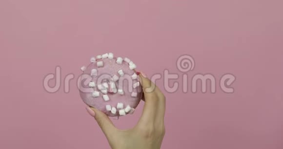 女人手里拿着粉红色美味可口洒在粉红色背景上的甜甜圈视频的预览图