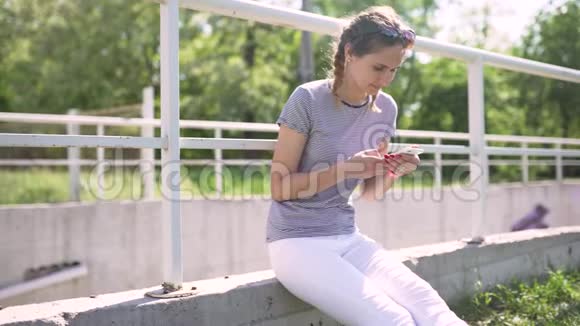 漂亮的年轻女子白天在公园里用手机视频的预览图