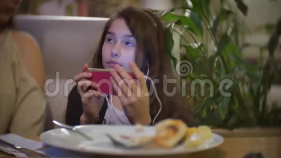 坐在快餐店里听智能手机音乐的少女在室内披萨咖啡馆吃饭的女婴视频的预览图