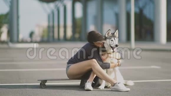 街上一个年轻漂亮的女人抱着她那只坐在滑板或长板上的哈士奇狗视频的预览图