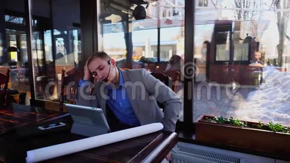 年轻的绘图员在咖啡馆通过平板电脑耳机电话和麦克风与客户交谈视频的预览图