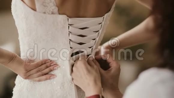 女性帮助新娘穿上礼服的近景婚礼前伴娘把婚纱系在后面视频的预览图