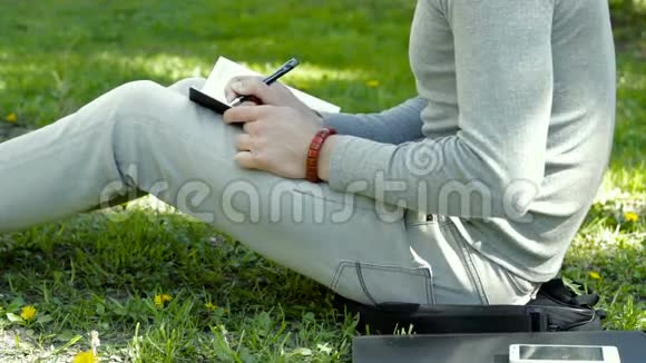 他坐在草地上的公园里在笔记本上写字视频的预览图