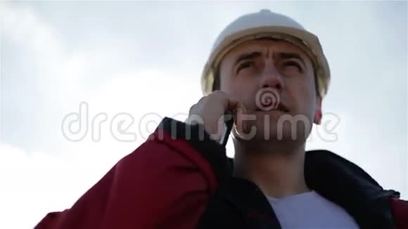 一个戴着白色头盔和红色夹克的建筑工人正在手机上交谈视频的预览图