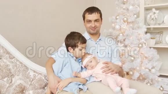年轻的父亲带着儿子和新生儿在圣诞节的沙发上视频的预览图