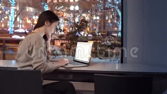 漂亮的年轻女商人坐在酒吧里用笔记本电脑工作在冬季夜晚的城市外装饰圣诞节视频的预览图