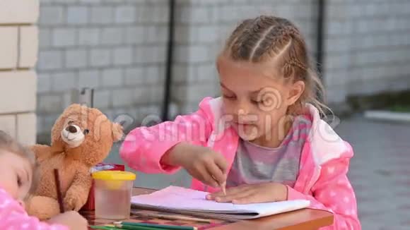 七岁的女孩热情地在相册上画一支铅笔和他的妹妹在街上画画视频的预览图