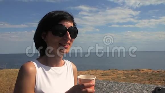 在灯塔的背景下女人在海边喝咖啡视频的预览图