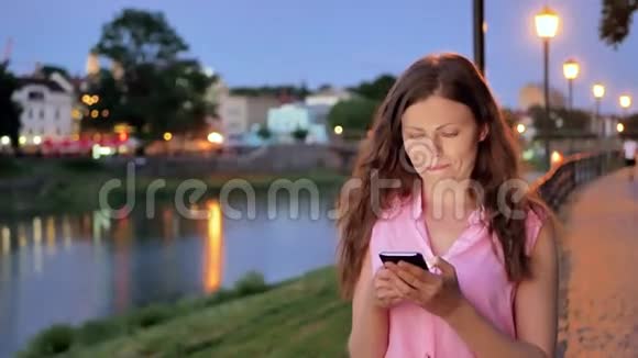 傍晚时分在海滨老城区河边和桥边使用智能手机的漂亮女孩视频的预览图