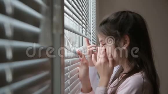 小女孩和男孩兄妹双胞胎从窗户透过百叶窗看着街道视频的预览图
