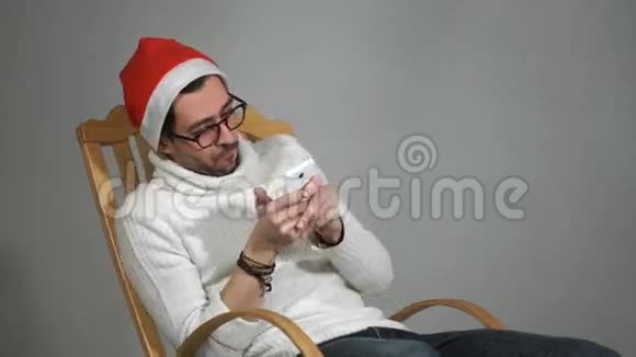 戴着眼镜和戴着红帽子的圣诞老人在你手机上玩游戏视频的预览图