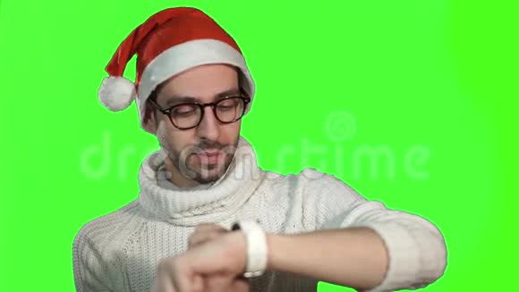 戴着圣诞老人帽子戴着智能手表在绿色背景下触摸屏幕的粗鲁严肃的人视频的预览图