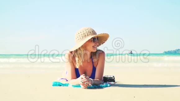穿着蓝色比基尼的年轻女子躺在海滩上带着老式相机戴着太阳帽视频的预览图