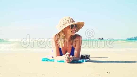 穿着蓝色比基尼的年轻女子躺在海滩上带着老式相机戴着太阳帽视频的预览图