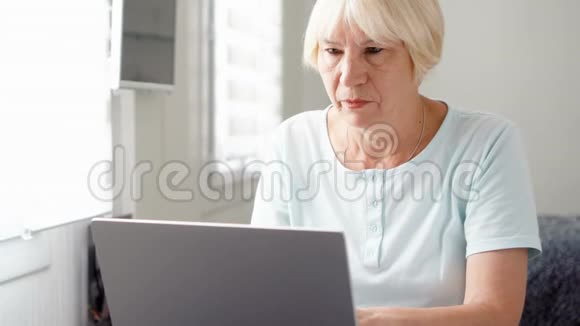 年长的金发女人在家里用笔记本电脑工作退休后的远程自由职业工作视频的预览图
