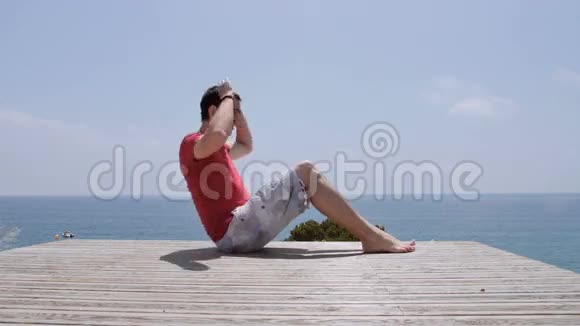 在阳光明媚的日子里运动型白种人在岩石海岸的海滩上泵腹视频的预览图