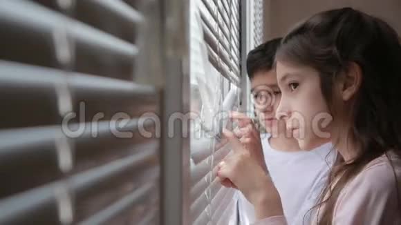 小女孩和男孩兄妹双胞胎从窗户透过百叶窗看着街道视频的预览图