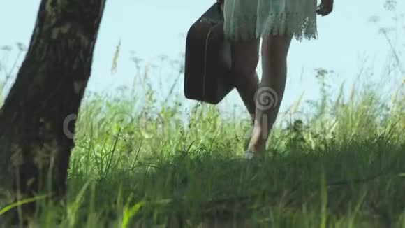一个带着手提箱的女孩在荒野的绿草上奔跑视频的预览图