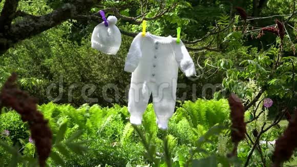 编织的白色婴儿紧身衣和帽子挂在花园的树枝上视频的预览图