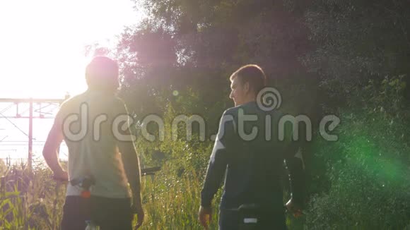 两个男朋友互相击掌在日落时骑自行车穿过森林小径朋友骑自行车视频的预览图