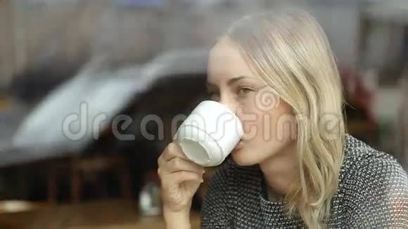 美丽的年轻女子在窗外喝着热咖啡做梦视频的预览图