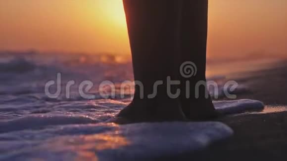 在美丽的夕阳下站在海边的年轻女子的脚慢动作3840x2160视频的预览图