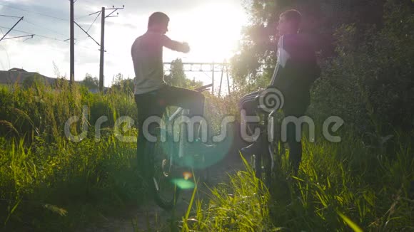 两个男朋友互相击掌在日落时骑自行车穿过草地朋友骑自行车视频的预览图