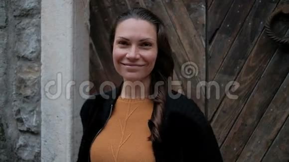 穿着橙色毛衣的年轻女子站在木门前微笑视频的预览图
