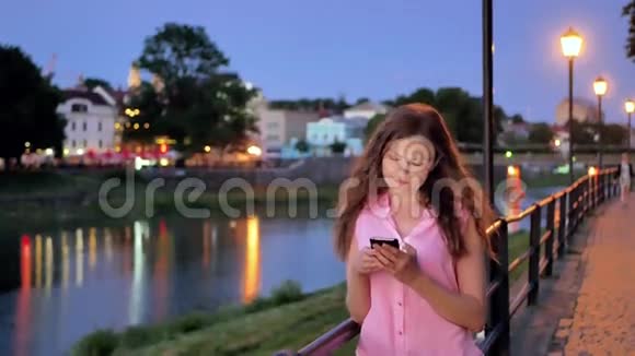 傍晚时分在海滨老城区河边和桥边使用智能手机的漂亮女孩视频的预览图