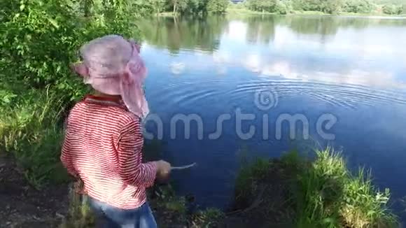 女孩把一根棍子扔进池塘的水中这个池塘位于老的杂草丛生的公园里视频的预览图