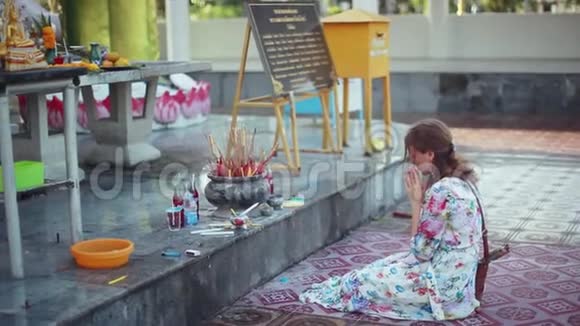年轻女子跪在寺庙里祈祷旁边是烧香棒和多臂钾女神视频的预览图