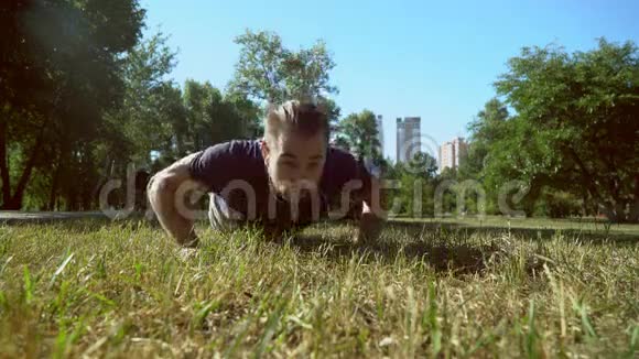 一个留胡子的年轻人正在草地上做俯卧撑视频的预览图