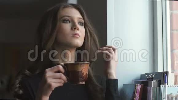 美丽的年轻模特站在窗户旁边喝咖啡视频的预览图