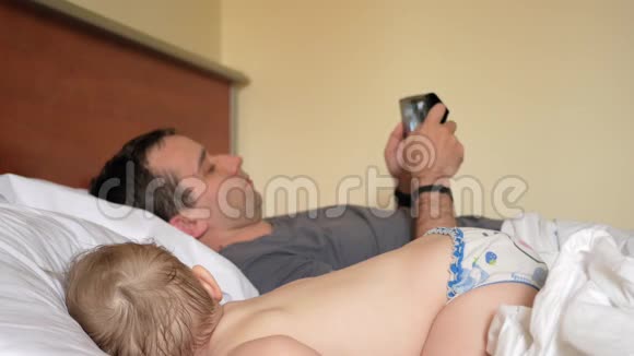 父亲在睡觉的婴儿附近的平板上读新闻一个男孩躺在床上房子的前景视频的预览图