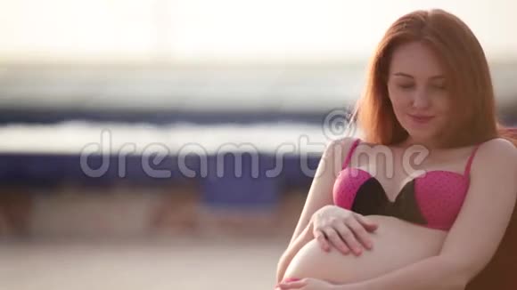 红头孕妇穿着泳衣在泳池边晒日光浴夏日心情视频的预览图