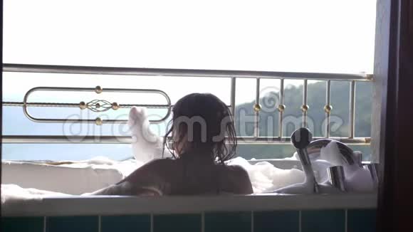 沐浴着年轻的黑发女人在泡沫的浴缸里放松在热带度假胜地享受美丽的海洋温泉视频的预览图