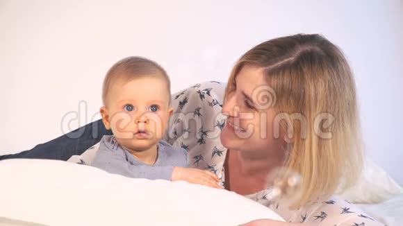有着蓝眼睛和金发的婴儿在床上和妈妈拥抱视频的预览图