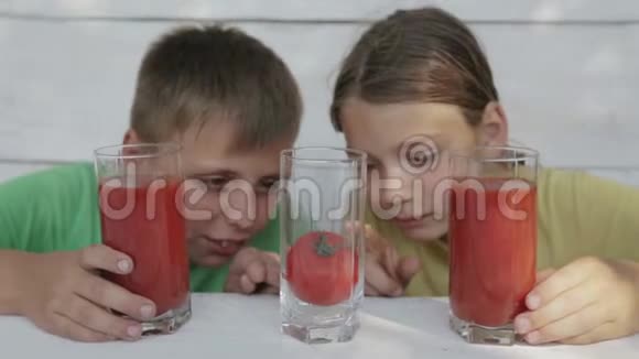 在白色背景下的孩子从玻璃杯中喝番茄汁两个男孩喝番茄汁视频的预览图