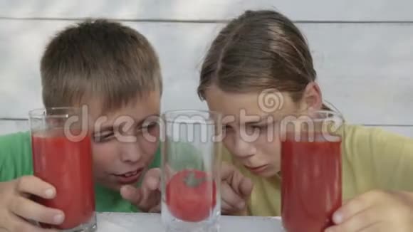 在白色背景下的孩子从玻璃杯中喝番茄汁两个男孩喝番茄汁视频的预览图