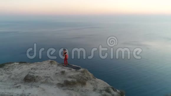 美丽的自由女子正在做瑜伽伸展在山顶与海景在日落空中镜头视频的预览图